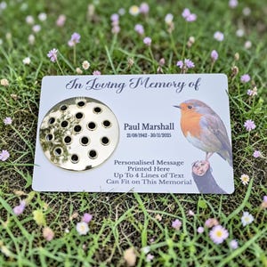May include: A memorial plaque with the text "In Loving Memory of" and the name "Paul Marshall" with dates. A gold-colored flower holder is on the left. A detailed illustration of a robin bird is on the right. The text "Personalised Message Printed Here" is also included.