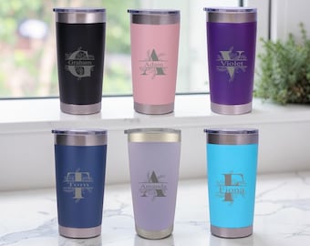 May include: Six personalized stainless steel tumblers in various colors: black, pink, purple, navy blue, lavender, and turquoise. Each tumbler features a name and initial design. The tumblers have a silver rim and lid.