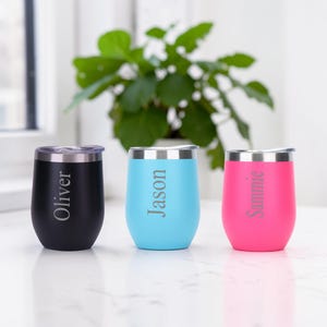 May include: Three stemless wine tumblers in black, light blue, and pink, each with a silver rim and lid. The black tumbler has "Oliver" engraved, the blue has "Jason", and the pink has "Sammie".