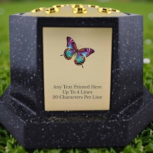 Puede incluir: Urna conmemorativa negra y dorada con imagen de mariposa. La urna tiene una textura moteada y una parte superior dorada con detalles circulares. Texto: Any Text Printed Here Up To 4 Lines 20 Characters Per Line.