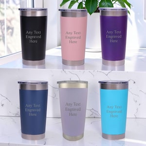 May include: Six stainless steel tumblers in black, light pink, purple, navy blue, lavender, and bright blue. Each tumbler features a clear lid and the engraved text Any Text Engraved Here centred on the front surface of the coloured body.