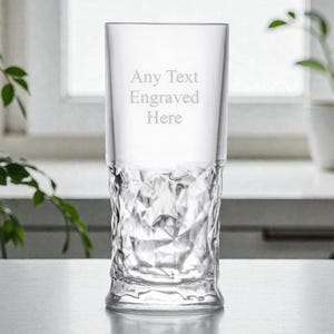 May include: A clear, engraved glass with a textured, diamond-like pattern on the lower half. The text "Any Text Engraved Here" is etched on the upper portion. The glass is tall and cylindrical, suitable for beverages.