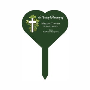 Könnte beinhalten: Ein grüner herzförmiger Gedenk-Gartenpfahl mit einem weißen Kreuz und grünen Blättern. Der Text lautet "In Loving Memory of Magaret Thomas 21/08/42 - 30/11/25 Gone But Never Forgotten".