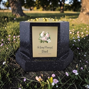 Peut inclure: Un urne funéraire en granit noir avec un dessus doré et une plaque décorative. La plaque présente deux colombes et l'inscription "In Loving Memory of Dad, Gone But Never Forgotten."