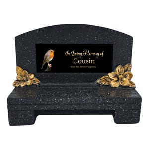 Könnte beinhalten: Schwarze Granit-Gedenkbank mit goldenen Akzenten. Sie hat eine zentrale schwarze Tafel mit einer Rotkehlchen-Illustration und dem Text "In Loving Memory of Cousin". Goldene Blumenverzierungen schmücken die Seiten.