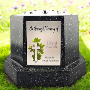 Puede incluir: Jarrón conmemorativo de granito negro con una placa plateada que dice "In Loving Memory of David 1945 - 2024 Gone But Never Forgotten". La placa tiene una cruz blanca y hojas verdes.