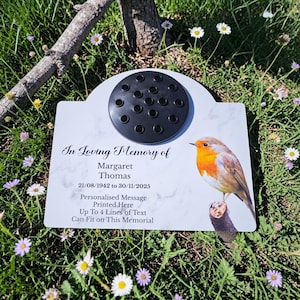 Peut inclure: Plaque commémorative blanche avec un motif marbré, comprenant un porte-fleurs noir et une illustration de rouge-gorge. Le texte indique "In Loving Memory of Margaret Thomas" avec des dates et un espace pour un message personnalisé.