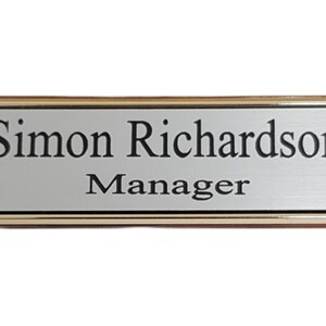 May include: A gold-framed nameplate with a silver background. The nameplate reads "Simon Richardson, Manager."