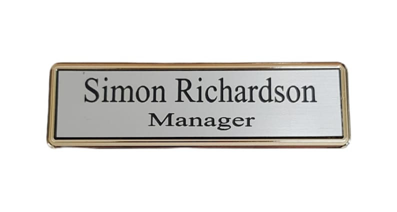 May include: A gold-framed nameplate with a silver background. The nameplate reads "Simon Richardson, Manager."