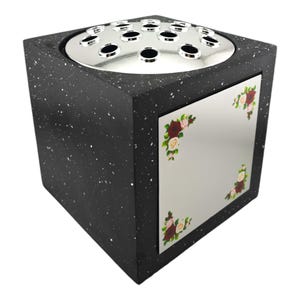 May include: A black speckled cube-shaped vase with a silver top featuring multiple holes for flower stems. A mirrored panel on the front is decorated with floral corner designs in red, pink, and green.