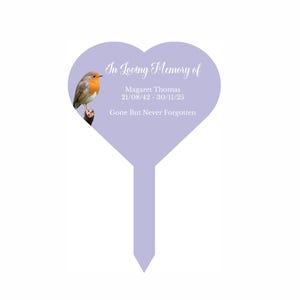 May include: A purple heart-shaped garden stake with a robin perched on a branch. The stake has the text "In Loving Memory of Magaret Thomas 21/08/42 - 30/11/25 Gone But Never Forgotten".