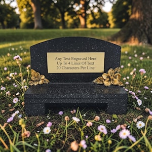 May include: Black granite memorial bench with a gold plaque inscribed with "Any Text Engraved Here Up To 4 Lines of Text 20 Characters Per Line." The bench features gold floral details and is set in a grassy area with flowers.