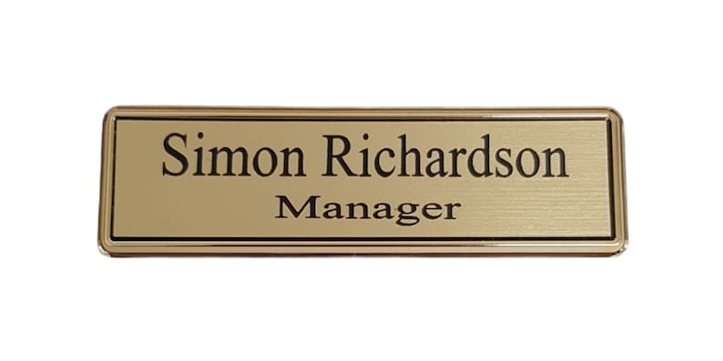 May include: Gold name tag with black text that reads "Simon Richardson Manager".