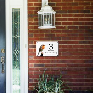 May include: White house number sign with a red robin perched on a branch. The sign reads "3 Main Street The Donaldson Family".