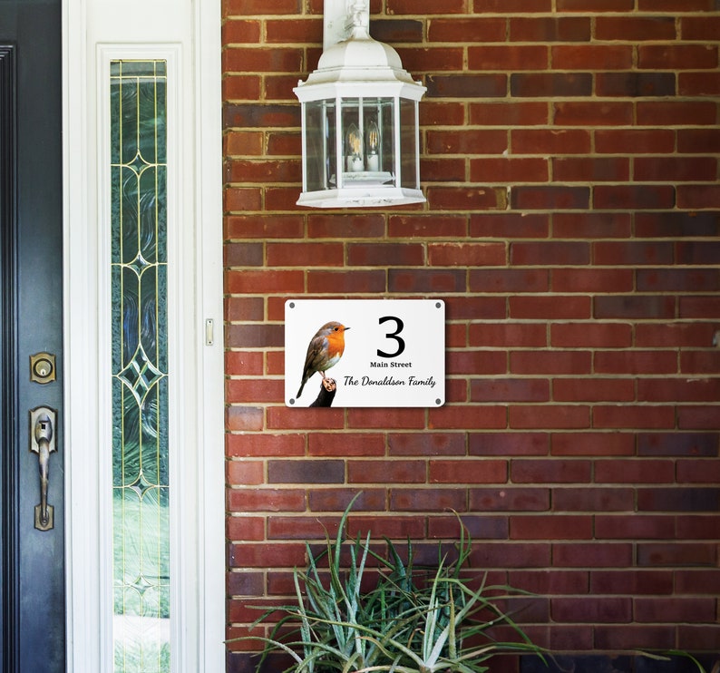 May include: White house number sign with a red robin perched on a branch. The sign reads "3 Main Street The Donaldson Family".