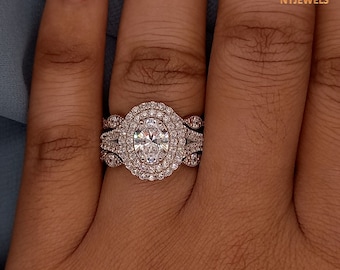 May include: A close-up of a woman's hand wearing a three-piece diamond engagement ring set. The centre stone is a large oval-shaped diamond surrounded by a halo of smaller diamonds. The band is a triple band with a twisted design.