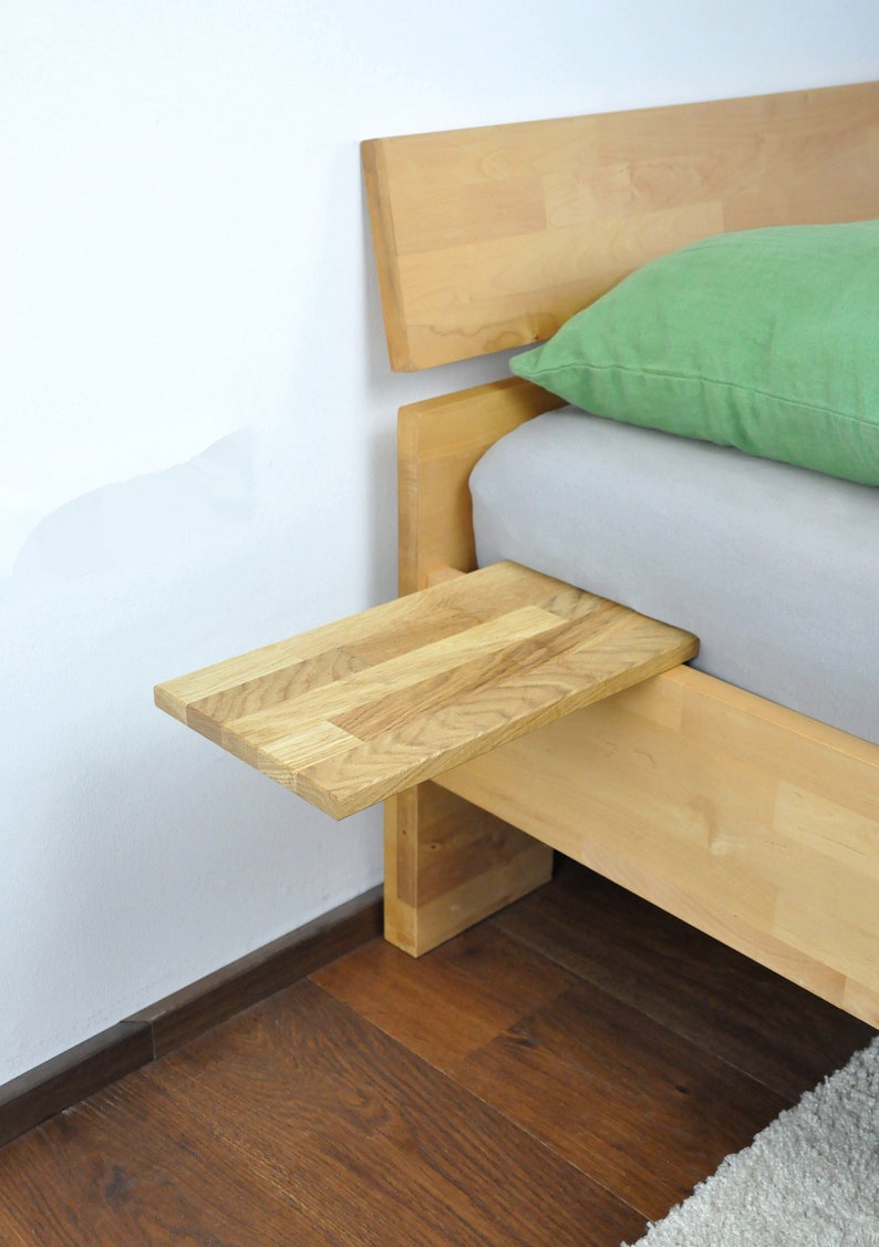 May include: A wooden bed frame with a light green pillow and a small wooden shelf attached to the side. The shelf is made of the same wood as the bed frame and is ideal for holding a book or a glass of water.