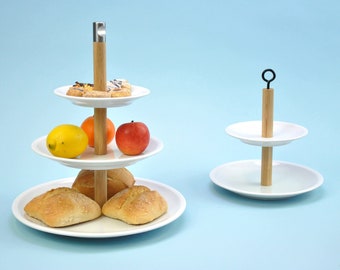 May include: A three-tiered white ceramic serving stand with a wooden centre pole. The top tier has pastries, the middle tier has fruit, and the bottom tier has bread rolls. A two-tiered white ceramic serving stand with a wooden centre pole is also shown.
