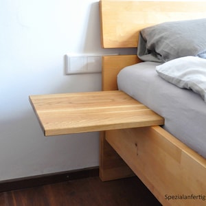 May include: A wooden bedside table with a light wood finish. The table is attached to the side of a bed and has a small shelf. The text "Spezialanfertigung 35 x 35 cm" is visible in the image.