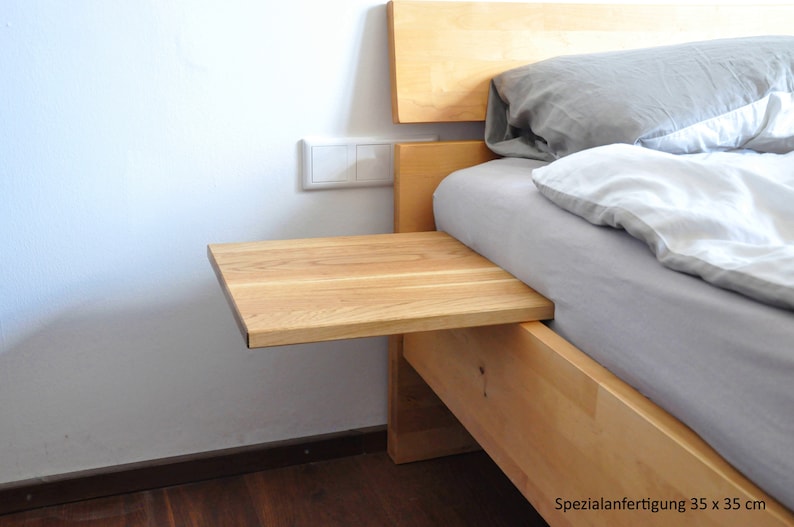 May include: A wooden bedside table with a light wood finish. The table is attached to the side of a bed and has a small shelf. The text "Spezialanfertigung 35 x 35 cm" is visible in the image.