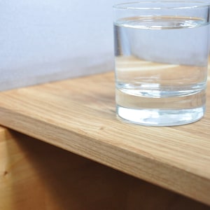 May include: A glass of water sits on a light wood bedside table with a drawer.