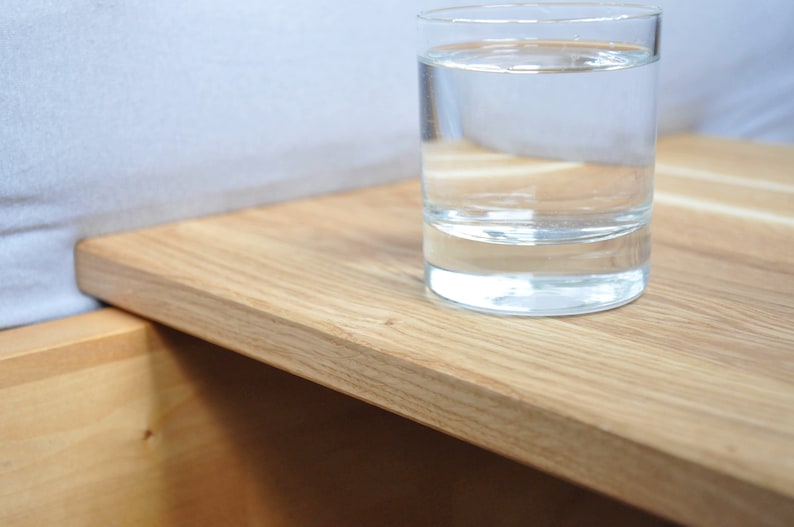 May include: A glass of water sits on a light wood bedside table with a drawer.