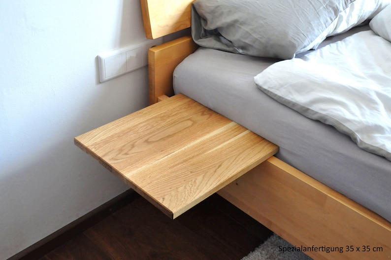 May include: A wooden bedside table with a light wood finish. The table is attached to the side of a bed and has a rectangular top that measures 35 cm by 35 cm.