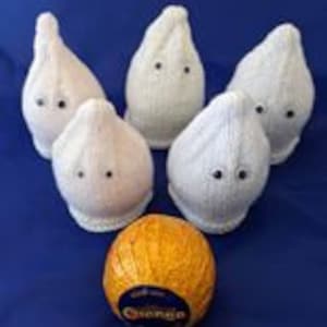 Könnte beinhalten: Fünf weiße gestrickte Geister-Ornamente mit schwarzen Augen, die ein goldenes Schokoladenei mit dem Aufdruck "Cadbury" umgeben.