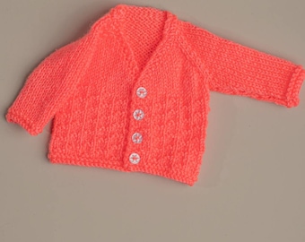 Handknitted cardigan in bright coral colour for 16 inch doll or medium premature baby. Acrylic yarn and machine washable