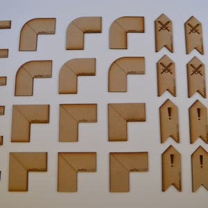 Könnte beinhalten: Set mit 20 Holzspielsteinen, darunter 16 Eckstücke in verschiedenen Größen und 4 Flaggenstücke mit unterschiedlichen Symbolen. Die Eckstücke sind mit "0,5" und "morfex.co.uk" beschriftet. Die Flaggenstücke haben Symbole von gekreuzten Schwertern und Ausrufezeichen.