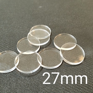 Peut inclure: Huit disques transparents en acrylique, chacun mesurant 27 mm de diamètre, sont disposés en forme de triangle sur une surface noire texturée.