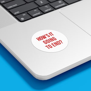 May include: A white laptop with a red sticker that says "HOW'S IT GOING TO END?" on the top right corner of the laptop.