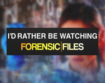 May include: A black rectangle with the text "I'D RATHER BE WATCHING FORENSIC FILES" in white and gold lettering. The background is blurred, with hints of blue and other colors.