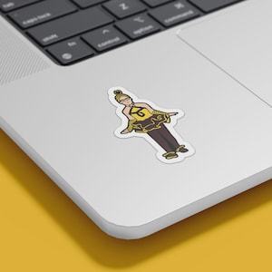 May include: A sticker featuring a cartoon illustration of a person in a yellow and brown outfit with the number 6 on the chest. The sticker is on a laptop, with a yellow background.