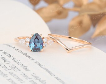 May include: A pear-shaped blue gemstone engagement ring with a halo of smaller diamonds set in rose gold. The ring is paired with a matching rose gold wedding band.