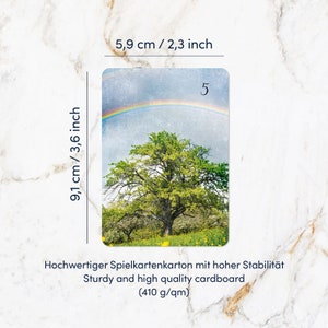K&ouml;nnte beinhalten: Eine rechteckige Spielkarte mit einem gr&uuml;nen Baum auf einer Wiese mit gelben Blumen unter einem Regenbogen und der Zahl 5. Die Karte misst 5,9 cm mal 9,1 cm und besteht aus stabilem 410 g/qm Karton, wie auf dem Text zu lesen ist.