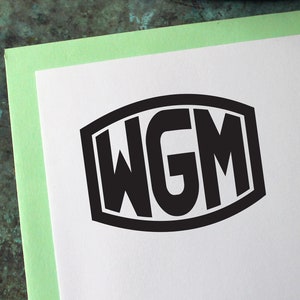 Op de afbeelding: Een witte envelop met een zwart WGM-monogram, een groene rand en een vintage postzegel met een berglandschap. Een houten potlood ligt bovenop. De postzegel leest "National Parks Center" en "Mount McKinley - Alaska".