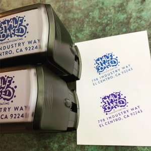 Pu&ograve; includere: Due timbri automatici neri con un logo blu e bianco che dice "Half Baked" e il testo "Powder Coating 798 Industry Way El Centro, CA 92243".
