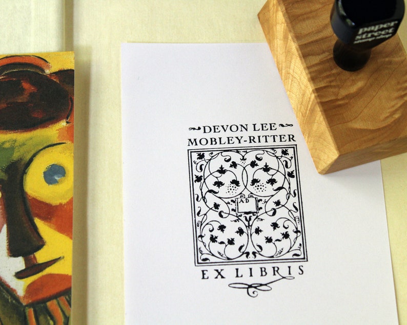 May include: Black and white bookplate stamp with a decorative design and the text "Devon Lee Mobley-Ritter Ex Libris".