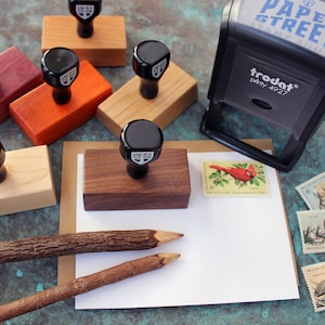 May include: A set of wooden stamps with a tree design, a Trodat stamp with the text "PAPER STREET STAMPS" and the text "trodat&reg; printy 4927", and two wooden pencils on a white card with stamps featuring wildlife conservation.