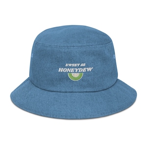 May include: A blue denim bucket hat with the text "SWEET AS HONEYDEW" embroidered on the front. The text is in white with a green melon slice graphic.