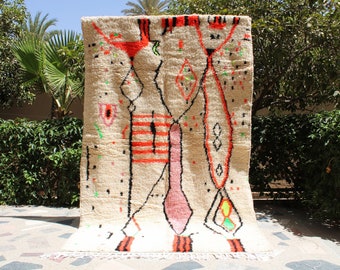 May include: A white rug with a geometric pattern in shades of red, pink, black, and green. The rug has a fringe border.