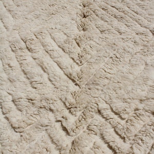 Puede incluir: Primer plano de una alfombra de color crema con un patr&oacute;n tejido texturizado. La alfombra tiene un sutil dise&ntilde;o en chevron.