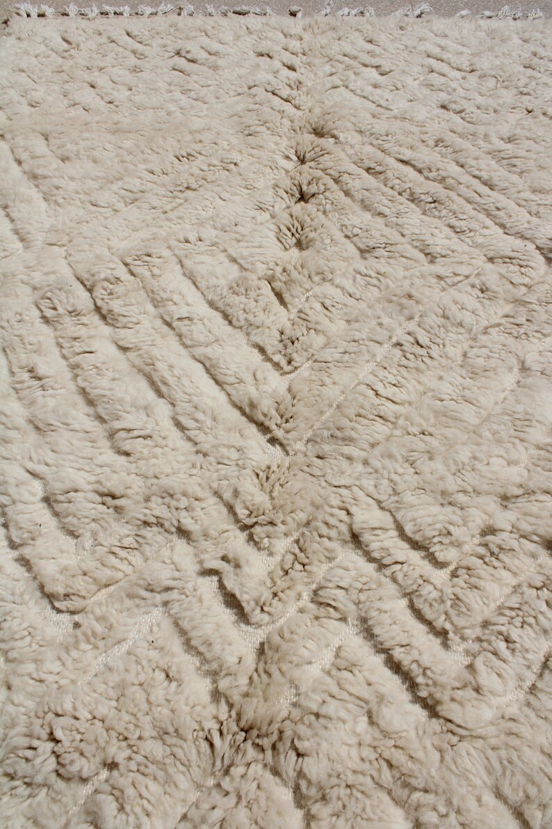 Puede incluir: Primer plano de una alfombra de color crema con un patr&oacute;n tejido texturizado. La alfombra tiene un sutil dise&ntilde;o en chevron.