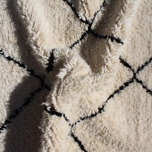 May include: A white and black Moroccan rug with a diamond pattern. The rug is made of wool and has a soft, fluffy texture.