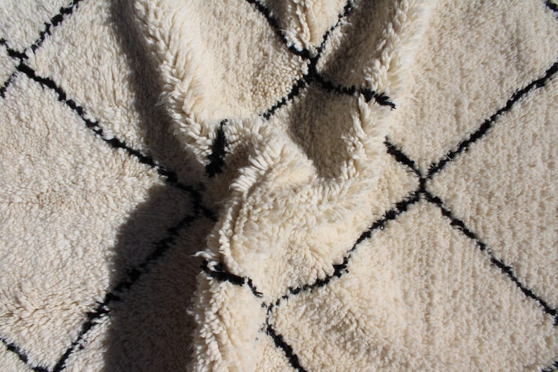 May include: A white and black Moroccan rug with a diamond pattern. The rug is made of wool and has a soft, fluffy texture.