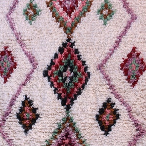 May include: A white rug with a repeating diamond pattern in shades of pink, green, brown, and black.