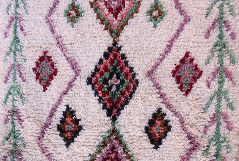 May include: A white rug with a repeating diamond pattern in shades of pink, green, brown, and black.