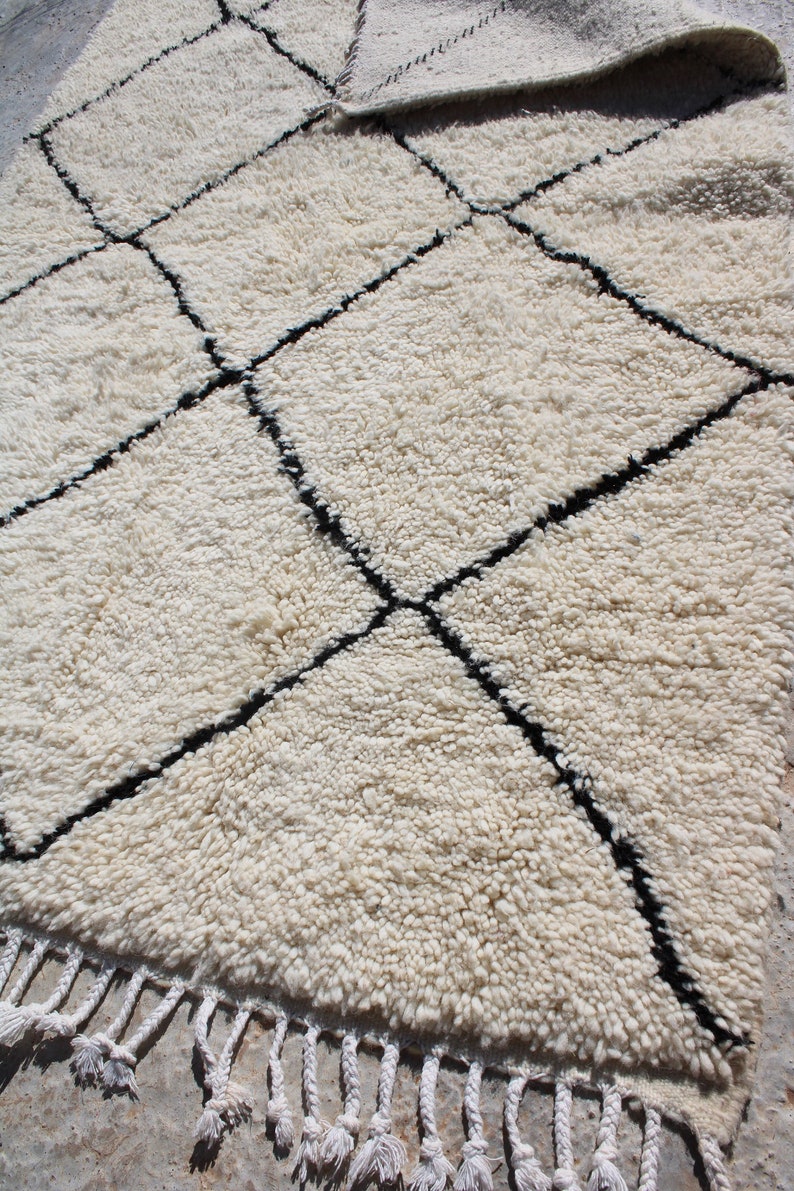 May include: White shag rug with a black diamond pattern. The rug has a fringe border.