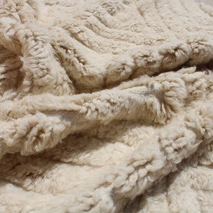 Puede incluir: Primer plano de una alfombra esponjosa de color crema con un patr&oacute;n tejido texturizado. La alfombra est&aacute; hecha de fibras naturales suaves y tiene una sensaci&oacute;n lujosa.
